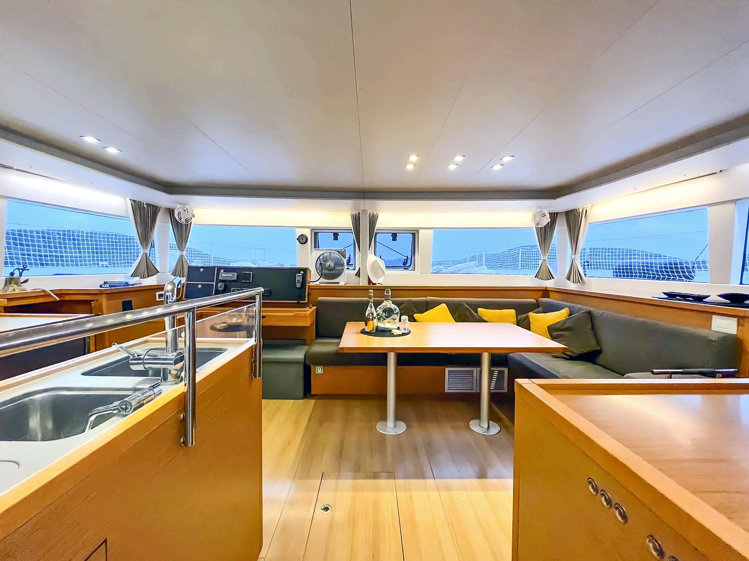 Interior de un yate con comedor, zona de estar con cojines, cocina y ventanas amplias que ofrecen vistas.
