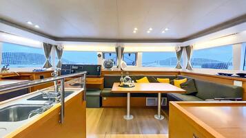 L’intérieur d’un yacht comprend un espace repas, un coin salon avec des coussins, une cuisine et de grandes fenêtres offrant une vue panoramique.
