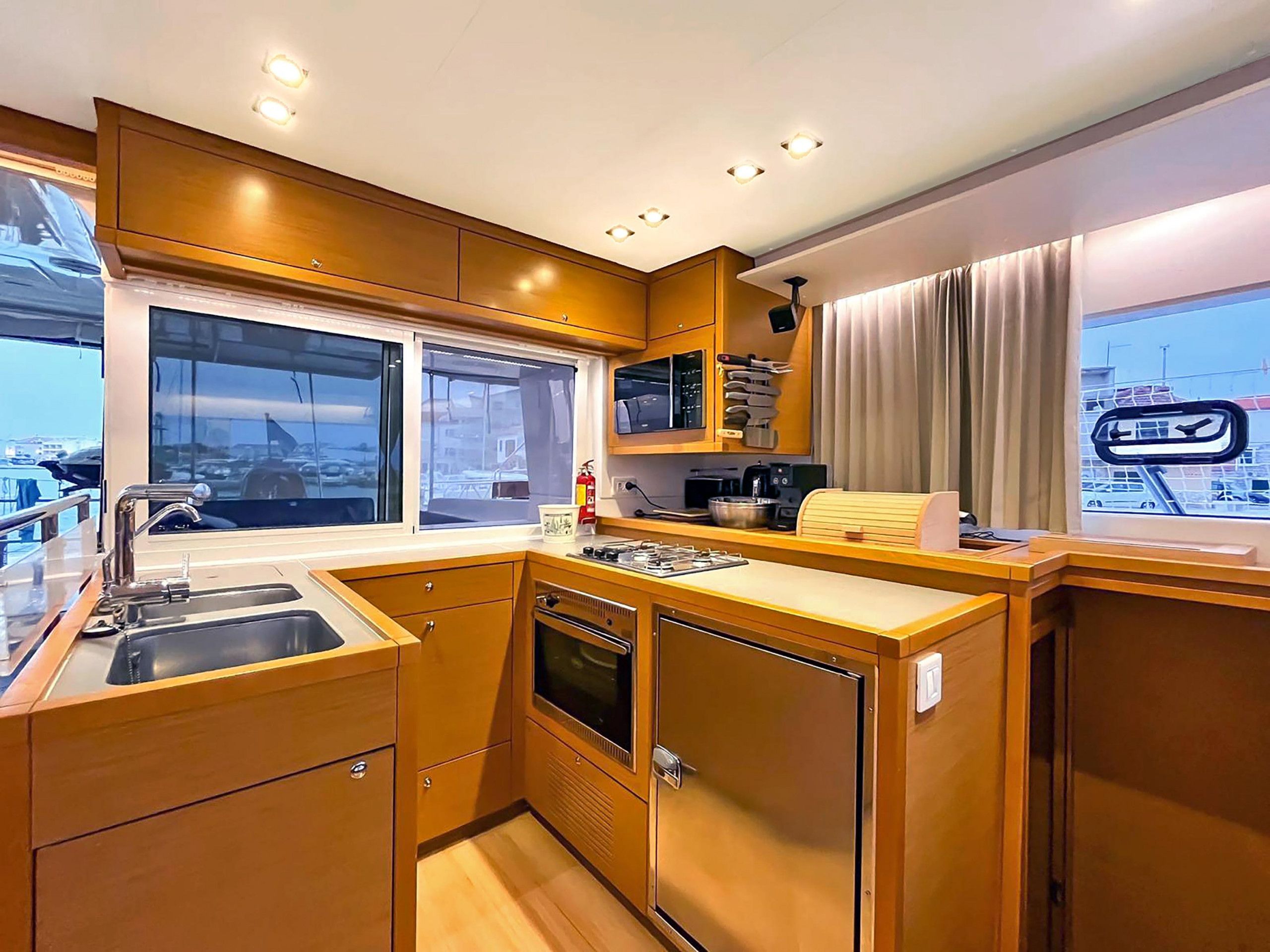 Cocina compacta con lavabo, estufa y horno, armarios de madera y ventana con vistas al puerto deportivo.