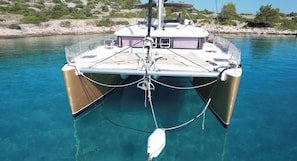 Ein Boot mit Kabine, Deck und einem Netzbereich, vor einer felsigen Küste in klarem, blauem Wasser verankert.