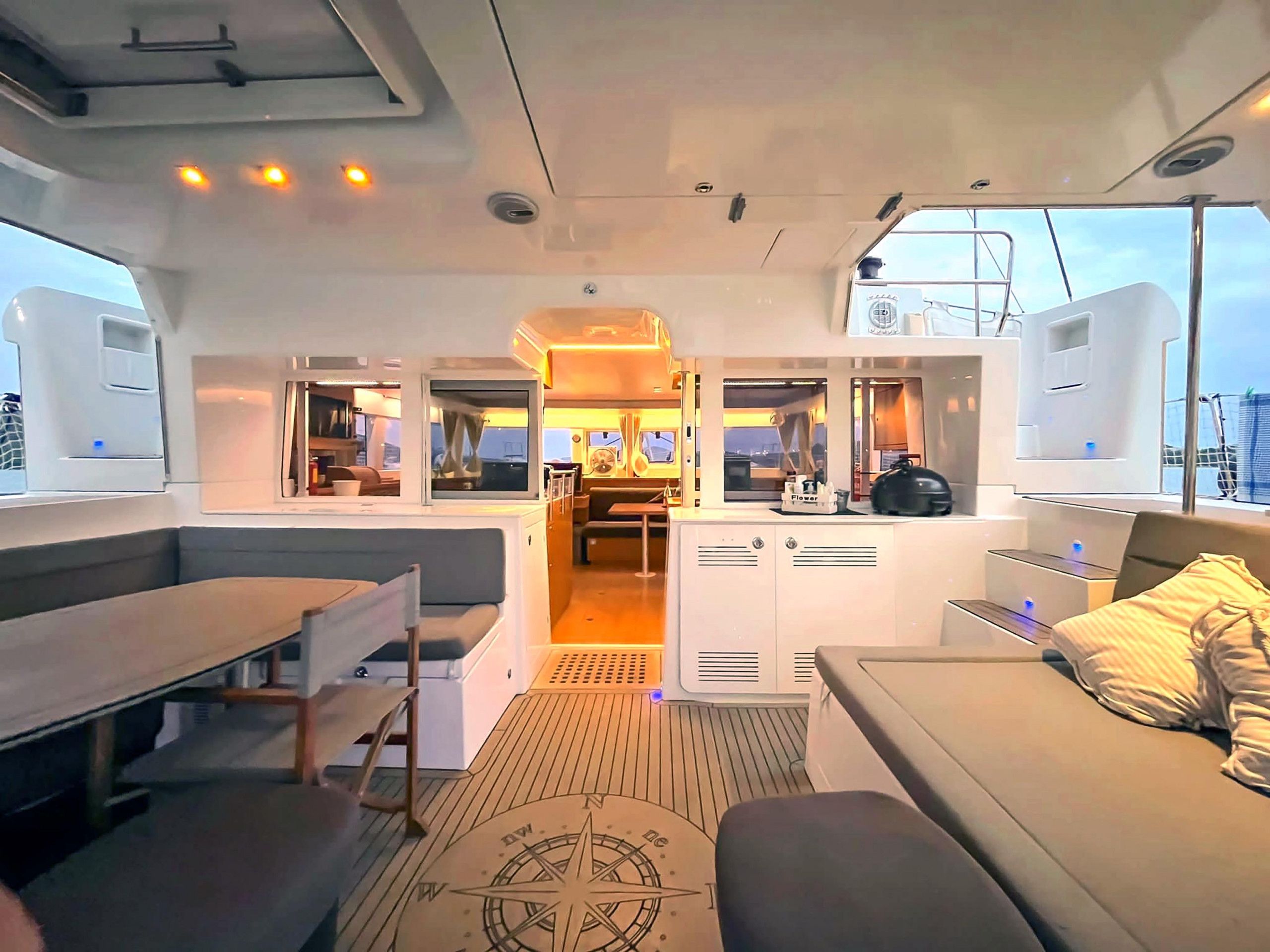 Interior de un barco con zona de comedor, cocina y área de estar con vista al mar.