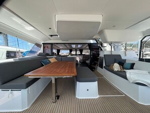 A boat's interior with a wooden table, cushioned seating, and a view of the marina. - Sun-kissed Sailing Adventure in Split-Dalmatia, Croatia (Seget Donji)