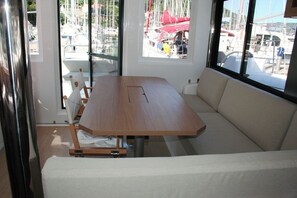 A room with a wooden table, a beige sofa, and large windows with a marina view. - Dubrovnik Delight: A Sun-Kissed Sailing Experience (Komolac)