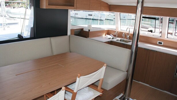 A compact galley with a wooden table and bench seating, a sink, and windows offering views of the marina. - Dubrovnik Delight: A Sun-Kissed Sailing Experience (Komolac)