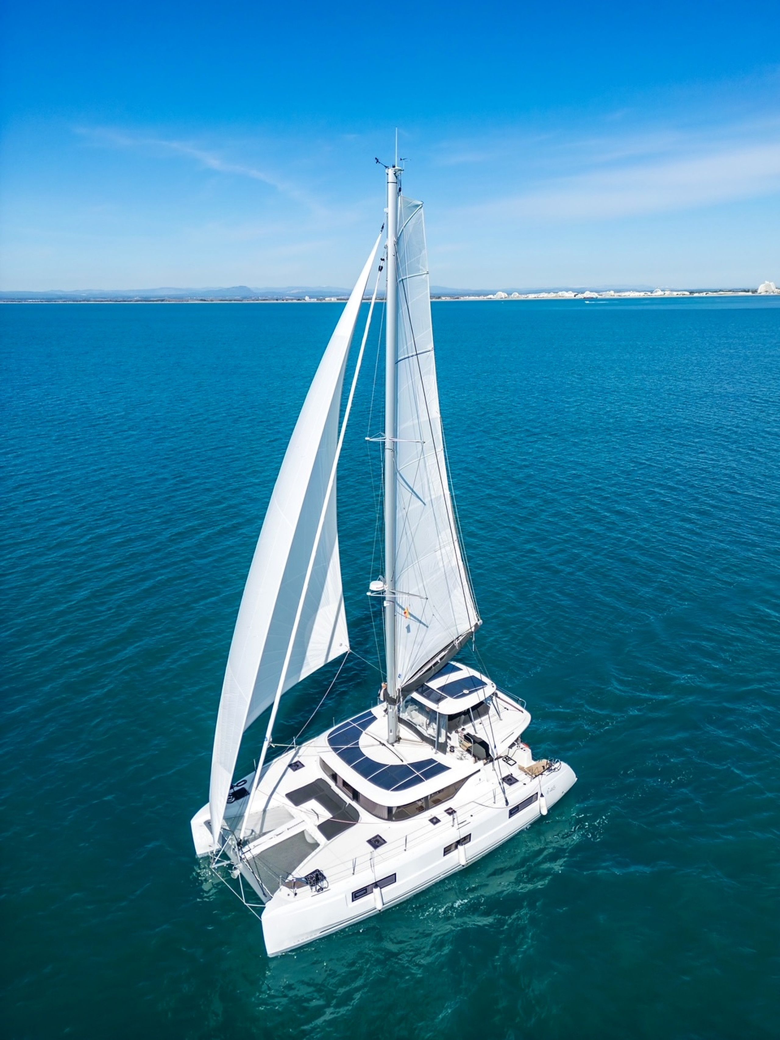Een zeilboot met een witte romp en meerdere zeilen, drijvend op kalm blauw water.