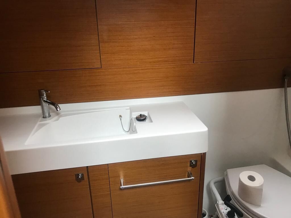 Une salle de bain avec un lavabo blanc, des meubles en bois, des toilettes et une poubelle.