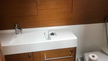 Ein Badezimmer mit einem weißen Waschbecken, Holzschränken, einer Toilette und einem Mülleimer.
