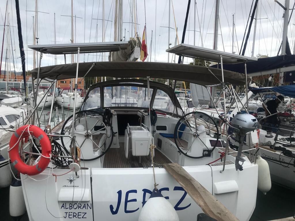 A marina with boats docked, including one with 'JEDZ' and 'ALBORAN JEREZ' visible on its side.