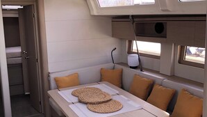 Um interior compacto e moderno com área de jantar, incluindo mesa e banco, um banco embutido com almofadas, uma pequena janela e um candeeiro fixado ao teto.