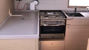 Uma cozinha compacta com fogão, forno e pia, uma tomada e uma janela acima da pia.