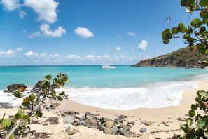 Une plage bordée d’une eau turquoise et limpide, un voilier et un paysage rocheux.