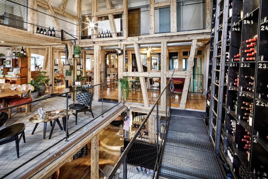 A multi-level interior with wooden beams, a mezzanine, and a wine rack.