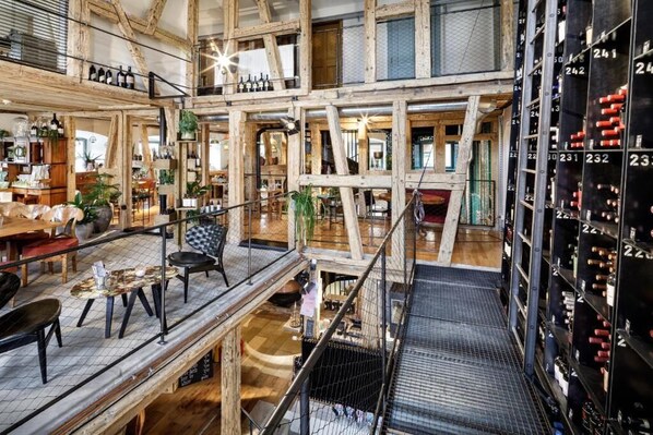 A multi-level interior with wooden beams, a mezzanine, and a wine rack.