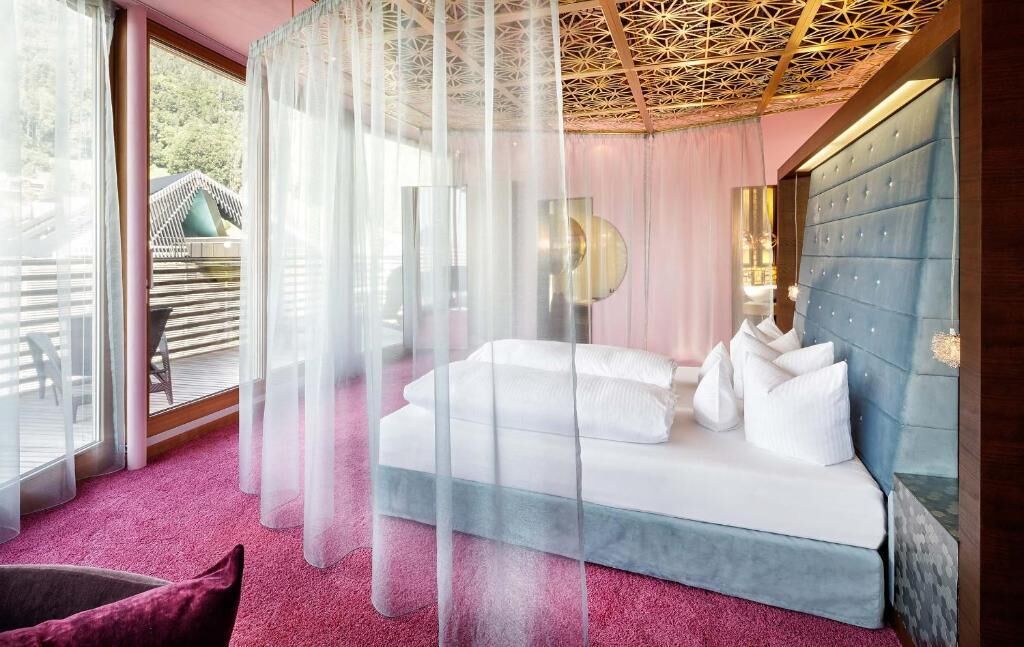 Un dormitorio con cama, un ventanal grande y vista a un edificio tradicional.