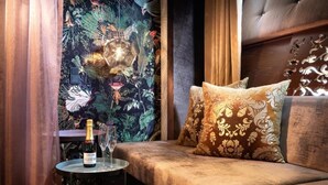 Una habitación con un sofá, una mesita redonda con una botella y un vaso, y una pared decorada con un mural floral.