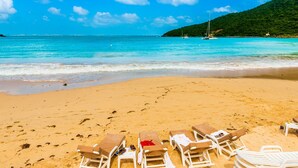 Una platja amb aigua turquesa cristal·lina, sorra daurada i diverses gandules disposades per prendre el sol.