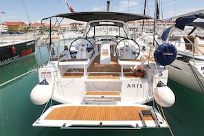 Ein Boot namens ARIS liegt in einer Marina mit Holzdeck, Steuerpult und einer Kabine mit Namensschild.