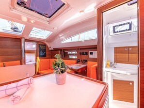 A yacht interior with a dining area, a small kitchen, and a seating area with orange cushions.