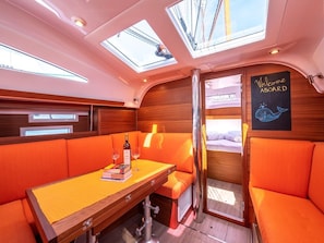 A cabin with a wooden interior, a table with a bottle and glasses, orange seating, and a 'Welcome Aboard' sign.