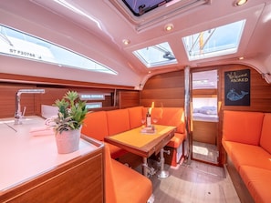 A yacht interior with a dining area, a potted plant, a welcome sign, and a bunkroom.