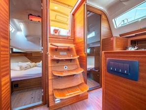A compact, well-lit interior with a bed, a built-in wooden shelf unit, and a control panel. - Sun-Kissed Sailing Adventure in Split, Croatia (Split)