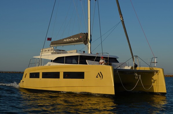 A yellow yacht with a cabin, a flag, and a logo on the bow.
