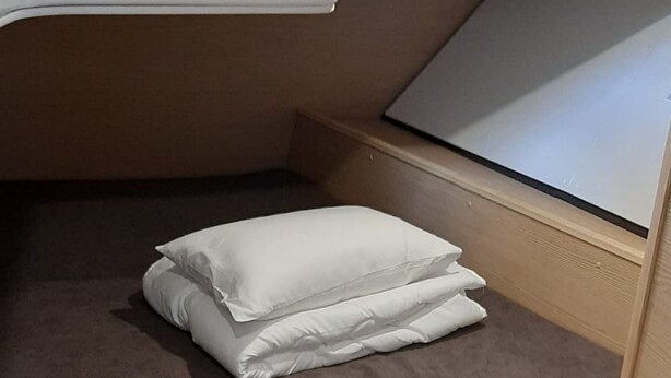 A compact bed with a pillow, a small wooden bench, and a striped floor. - Sun-kissed Sailing Adventure in Split-Dalmatia, Croatia (Trogir)