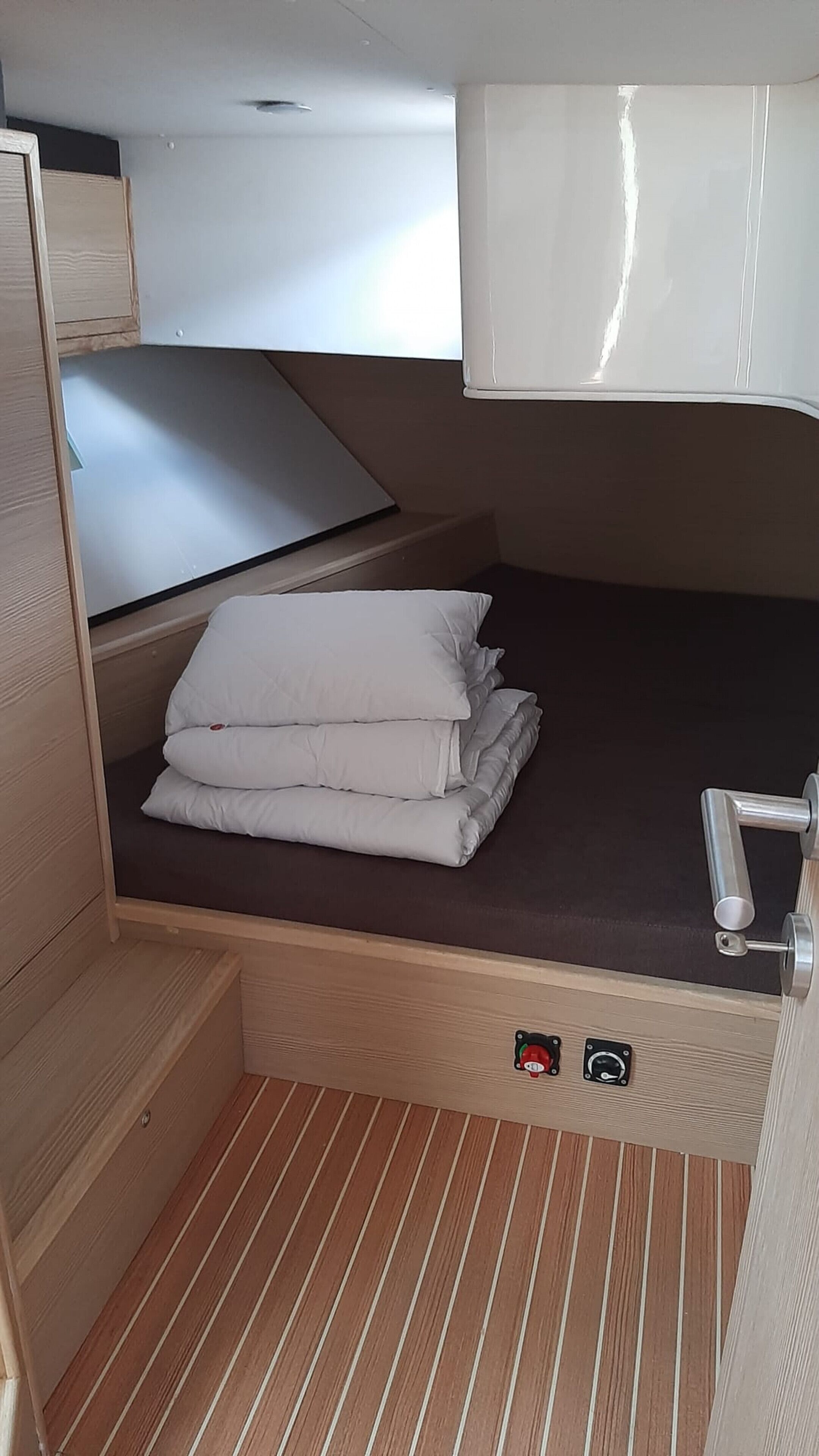 Una habitación pequeña y bien iluminada con una cama, un área de descanso y una puerta con manija.
