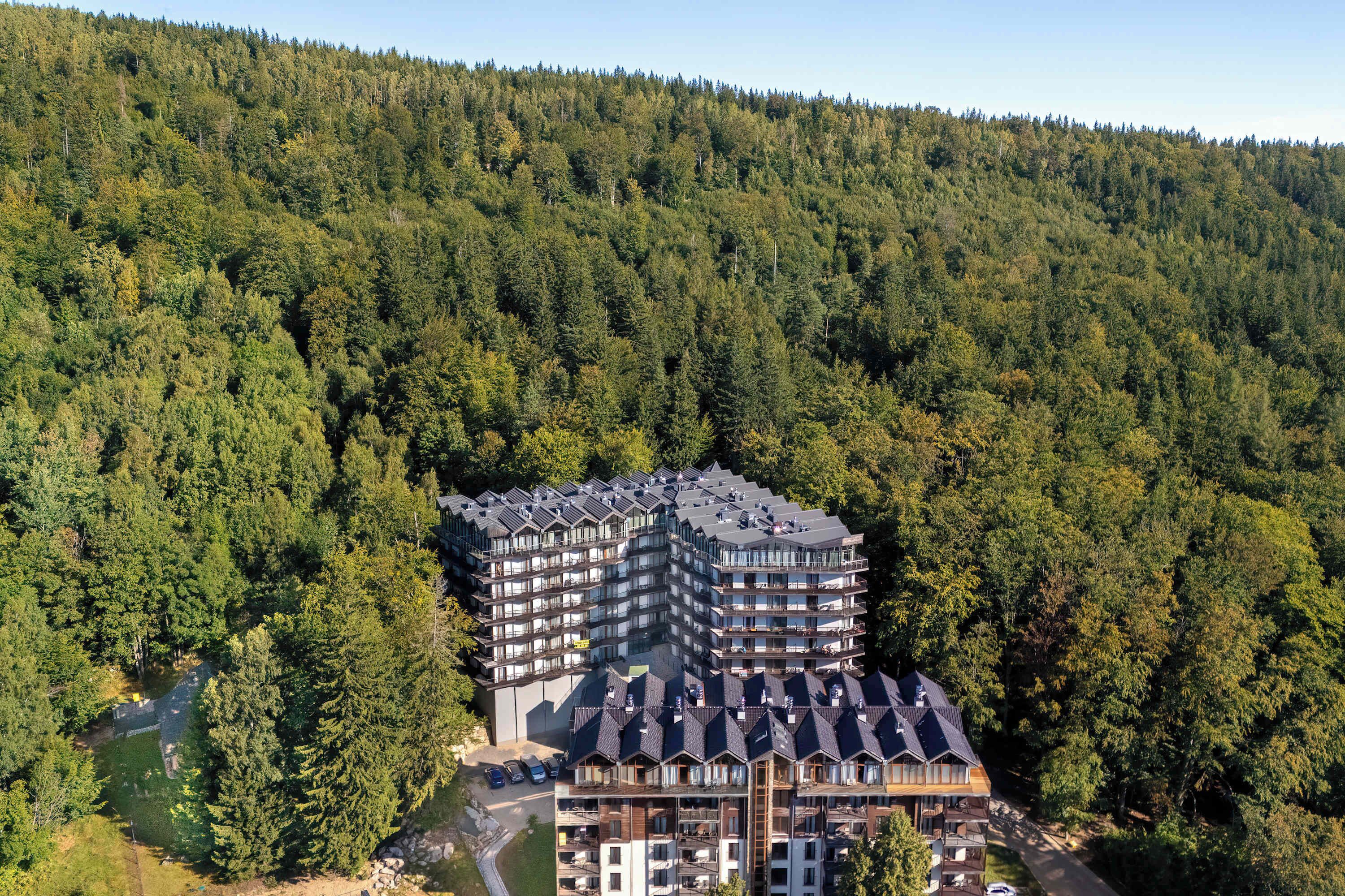 An aerial view of the apartment building surrounded by dense forest. The location provides beautiful natural scenery.