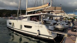 Eine Yacht liegt in einer Marina festgemacht, mit dem Namen 'Lucio 40' und einem Banner 'DreamYachtCharter' auf dem Deck.