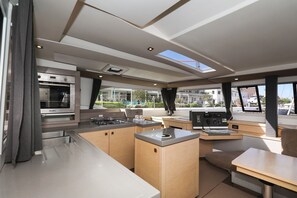 A modern kitchen with a built-in oven, a gas stove, and a dining area with a table and bench. - Sun-kissed Sailing Adventure in Split-Dalmatia, Croatia (Trogir)