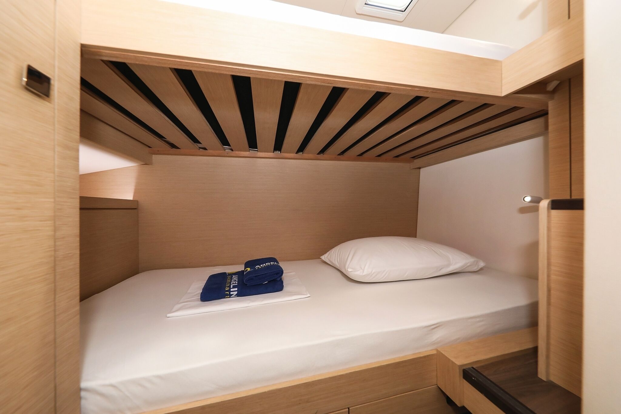 A compact, wooden bunk bed with a skylight, a white pillow, and neatly folded blue clothing on the bed.