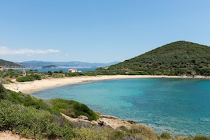 Un paysage côtier caractérisé par une eau d’un bleu limpide, une plage de sable et une colline couverte d’une végétation luxuriante.