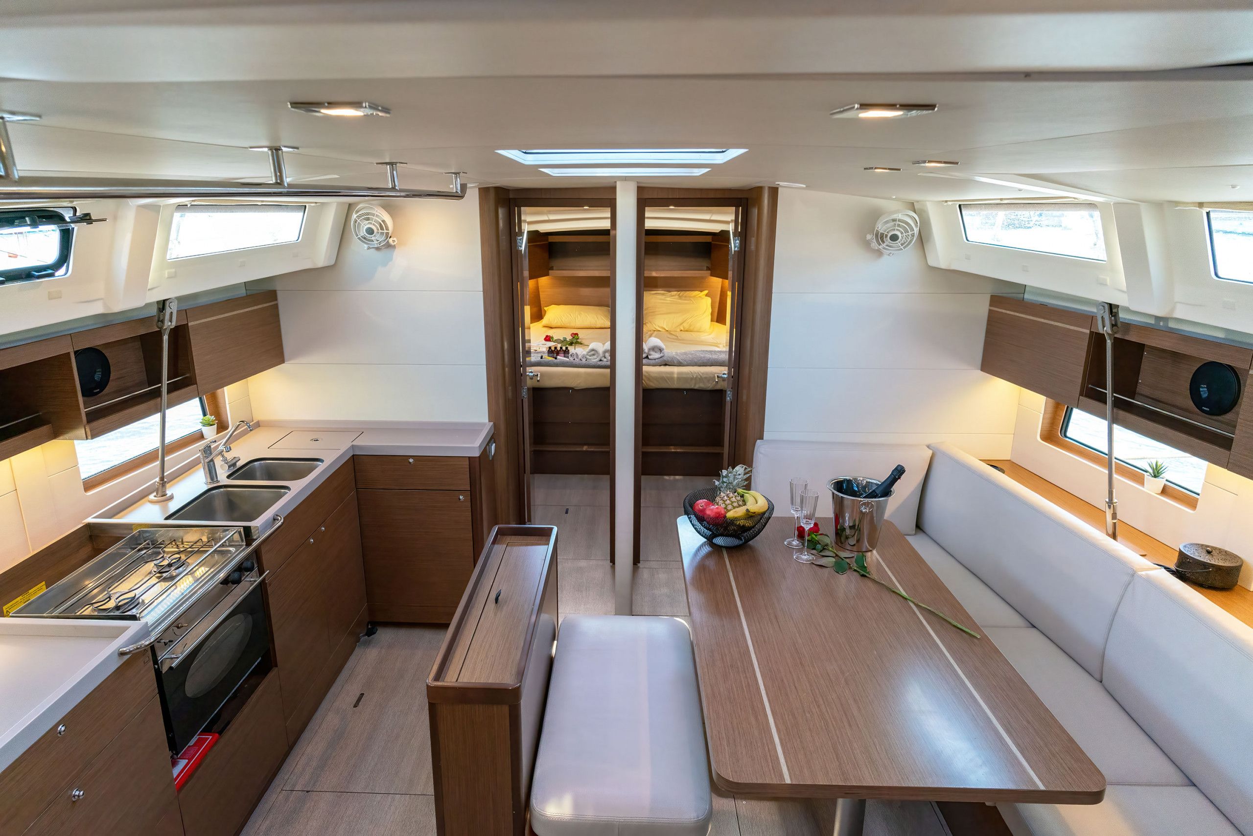 A compact kitchen with a stove, sink, and storage cabinets. There is a dining area with a bench and a table, and a small seating area with a bench.