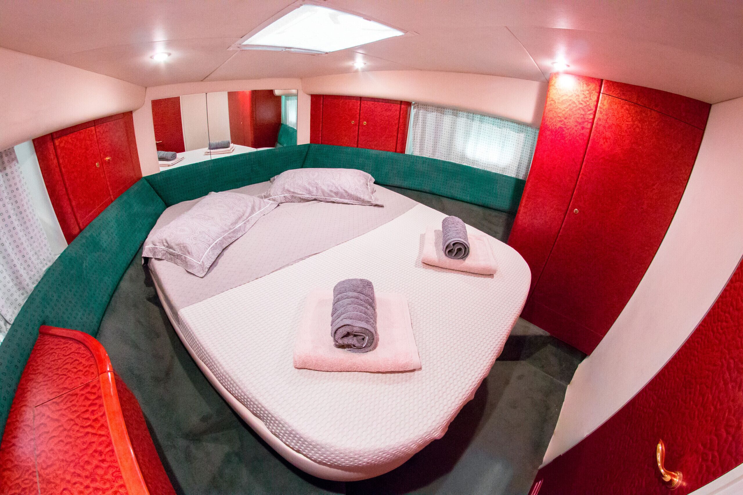 Ein Zimmer mit einem gebogenen Bett, roten und grünen Wänden, einem großen Spiegel und einer Deckenleuchte.