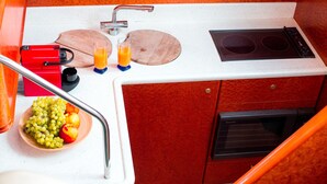 A compact kitchen with a sink, two wooden cutting boards, a red appliance, a glass of orange juice, a bowl of fruit, and a microwave. - Sun-Kissed Sailing Adventure in the Stunning Islas Cícladas (Paros)