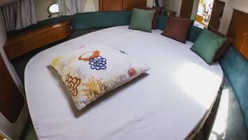 Una cama con almohada estampada, cabecera tapizada de verde y un mueble de madera.