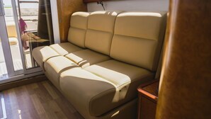 A beige sofa in a room with a wooden floor and a glass door leading outside. - Sun-Kissed Sailing Adventure in the Stunning Islas Cícladas (Paros)