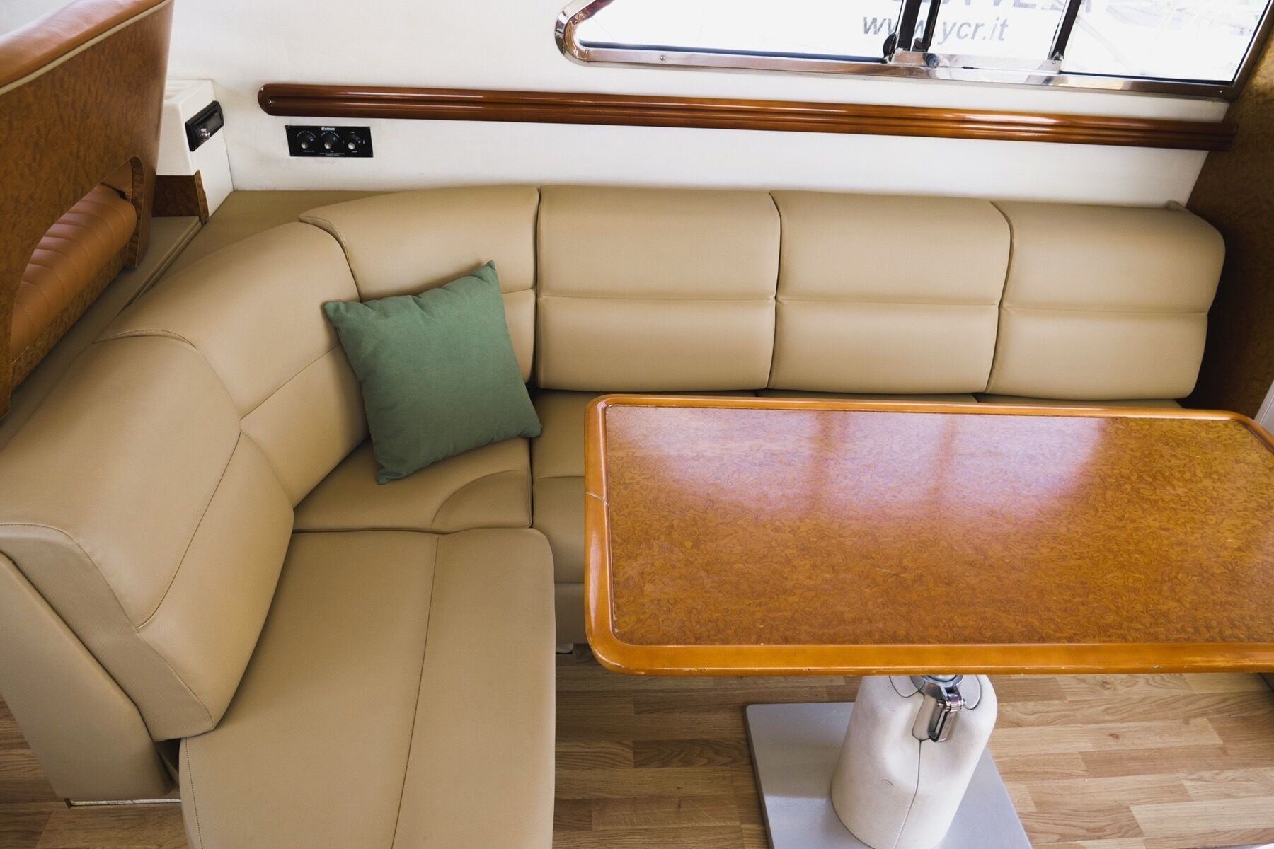 Interior de barco con un sofá tapizado en color beige, un cojín verde y una mesa de madera.