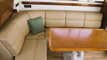Interior de barco con un sofá tapizado en color beige, un cojín verde y una mesa de madera.