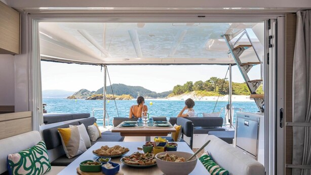 Ein Essbereich auf einem Boot mit einem für zwei Personen gedecktem Tisch, mit Blick auf eine Küstenlandschaft.