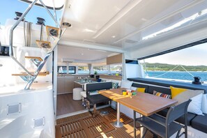 A yacht interior with a dining area, kitchen, and seating by the window overlooking the sea. - Sun-Kissed Sailing Adventure in the Ionian Islands, Lefkada (Lefkada)