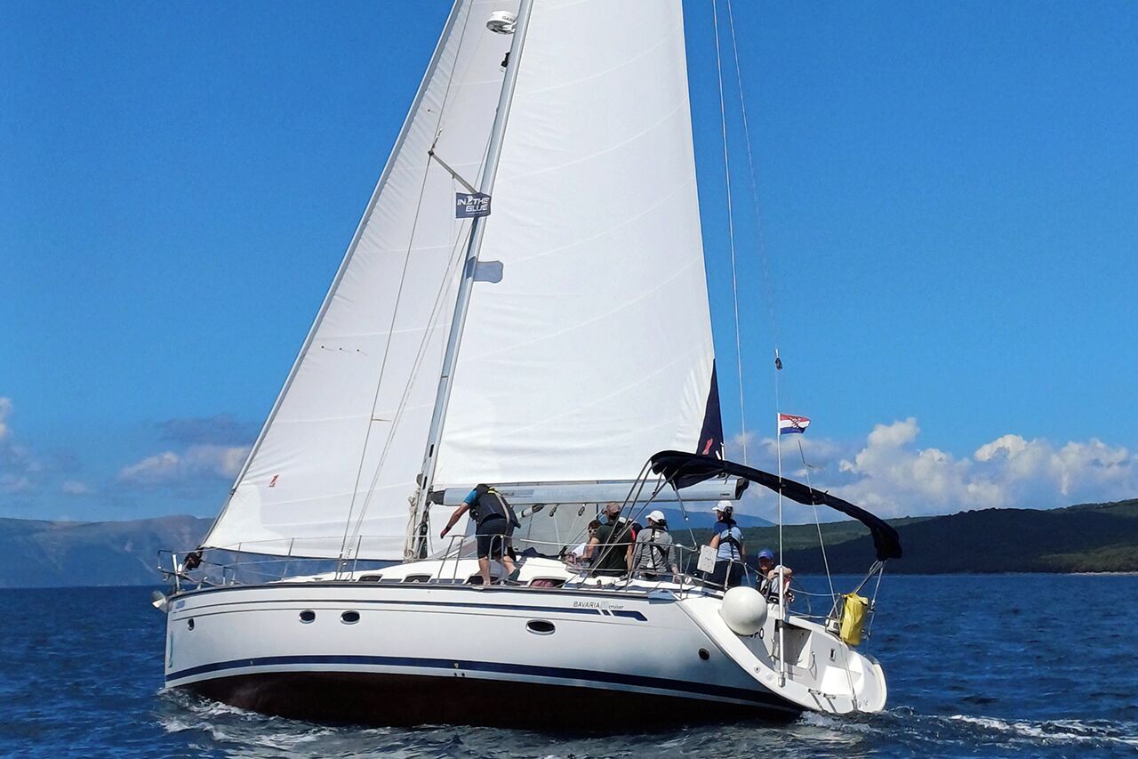 Eine Segelyacht mit weißem Rumpf und Besatzung an Bord.