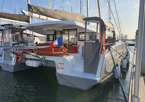 Eine Yacht liegt in einer Marina vor Anker, mit überdachter Terrasse, Sitzgelegenheit und einer Flagge.