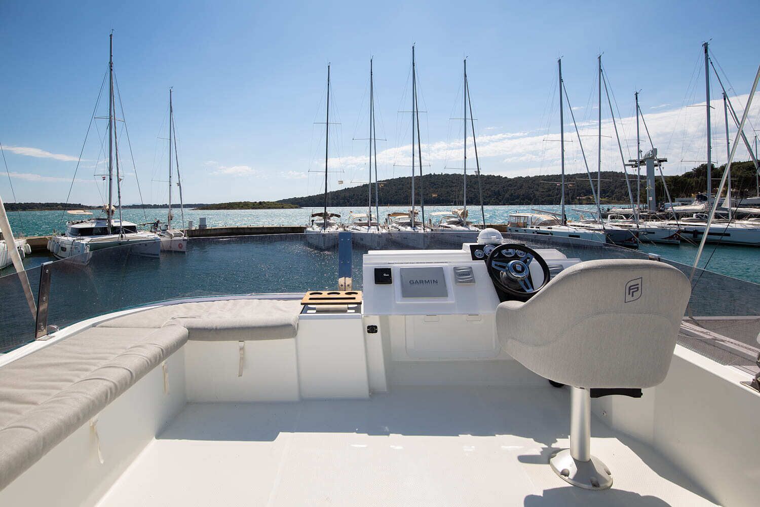 Interior de un barco con un sistema de navegación Garmin, un asiento acolchado y vista a un puerto deportivo con varias embarcaciones amarradas.