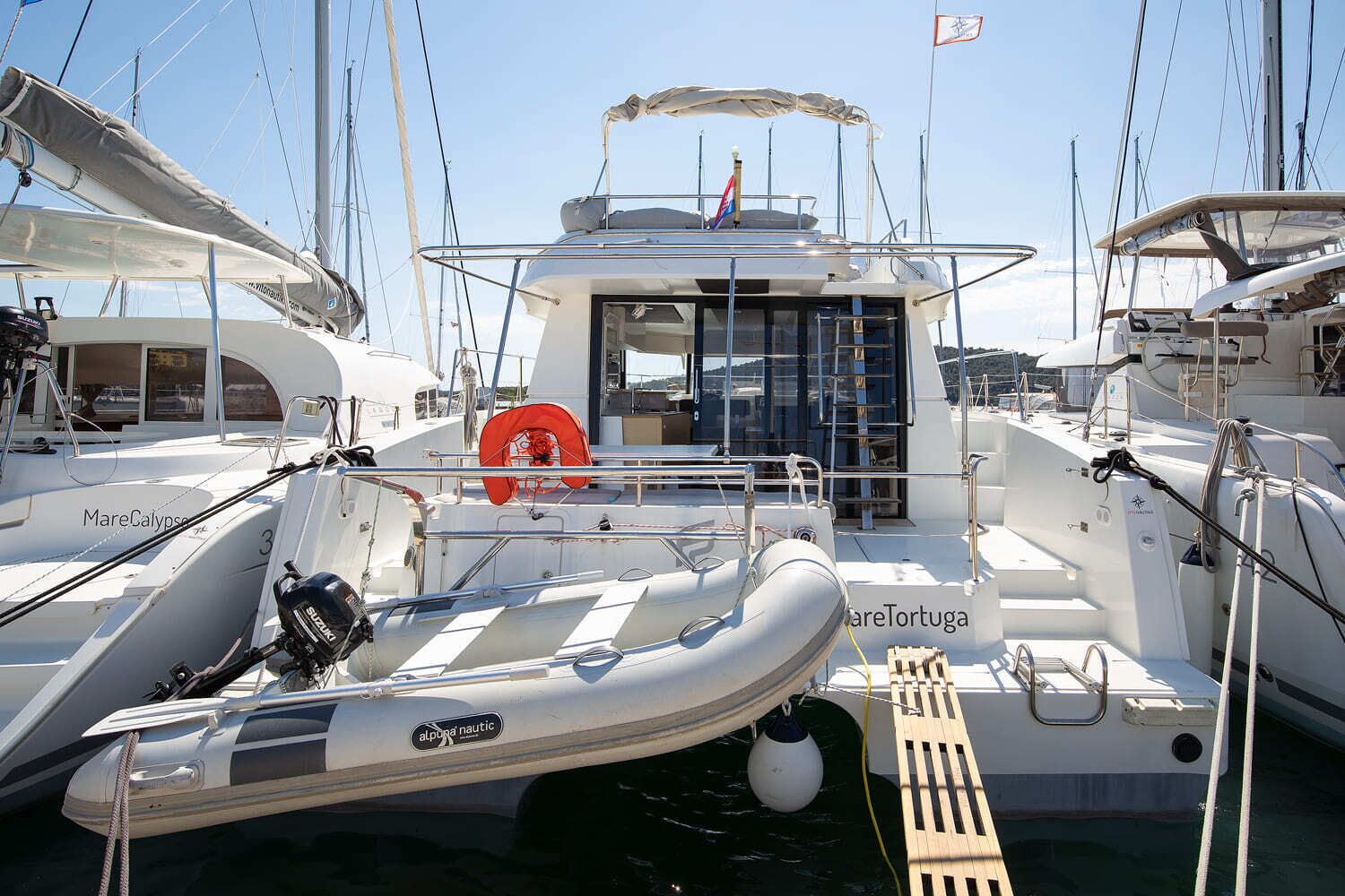 A marina with several boats docked, including a white boat with 'MareCalypso' and 'alpina nautical' visible.