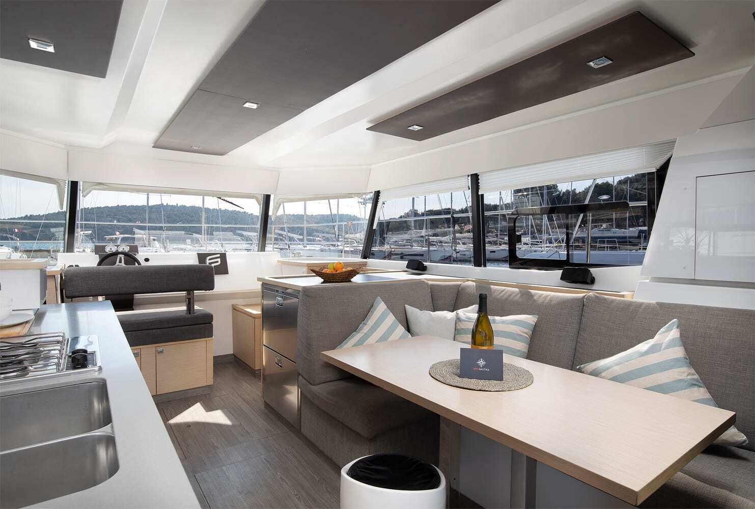 Interior moderno de iate com área de refeições, assentos e vista para o porto de iates.