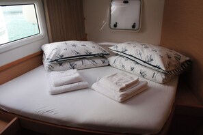 Un letto rifatto con lenzuola bianche e cuscini decorati, una finestra con tende e un interruttore della luce fissato al muro.