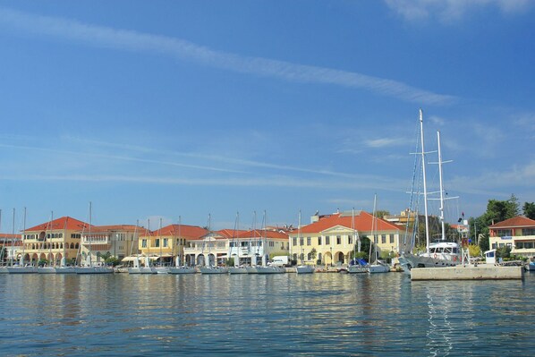 A marina with multiple boats docked, a large sailboat, and buildings with red roofs.