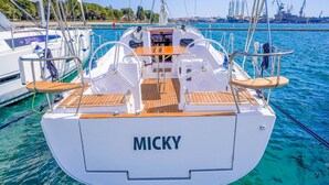 Puukantisella ja metallikaiteilla varustettu purjevene nimeltä ’MICKY’ oli ankkuroituna satamaan, jossa vesi oli kirkkaan sinistä ja taustalla näkyi teollisuusrakennuksia.